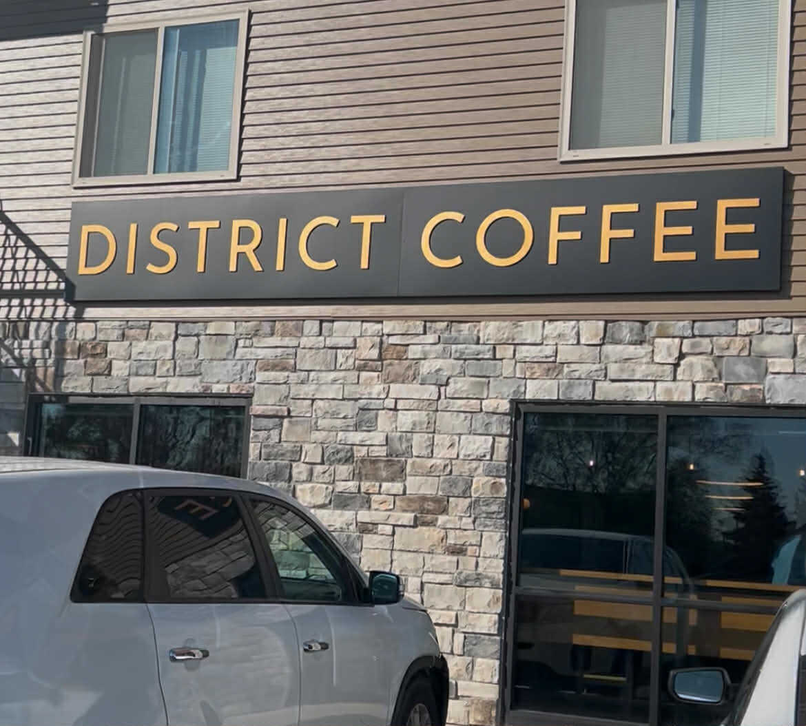 Exterior sign of District Coffee in St. Cloud MN with stone façade and parked cars in front.